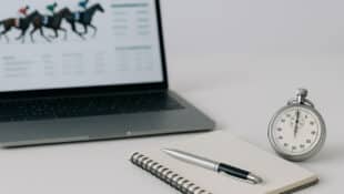 An open laptop, a notebook and pen on a table.