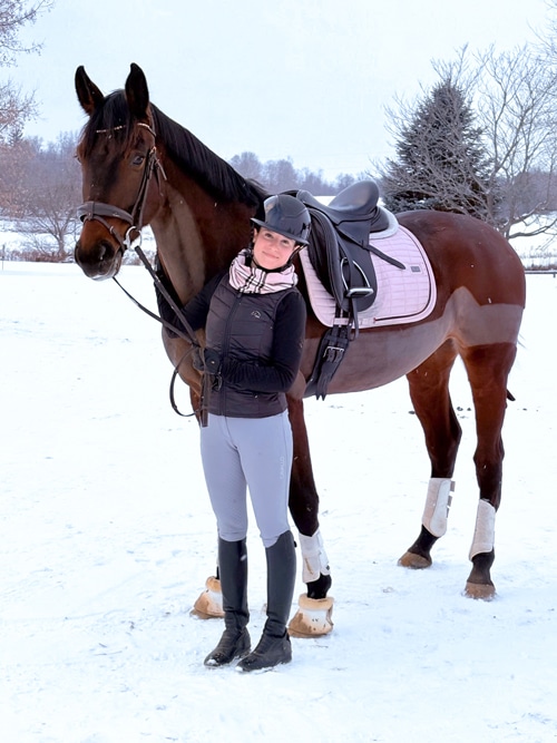 A woman holding a bay dressage horse in a snowy field.
