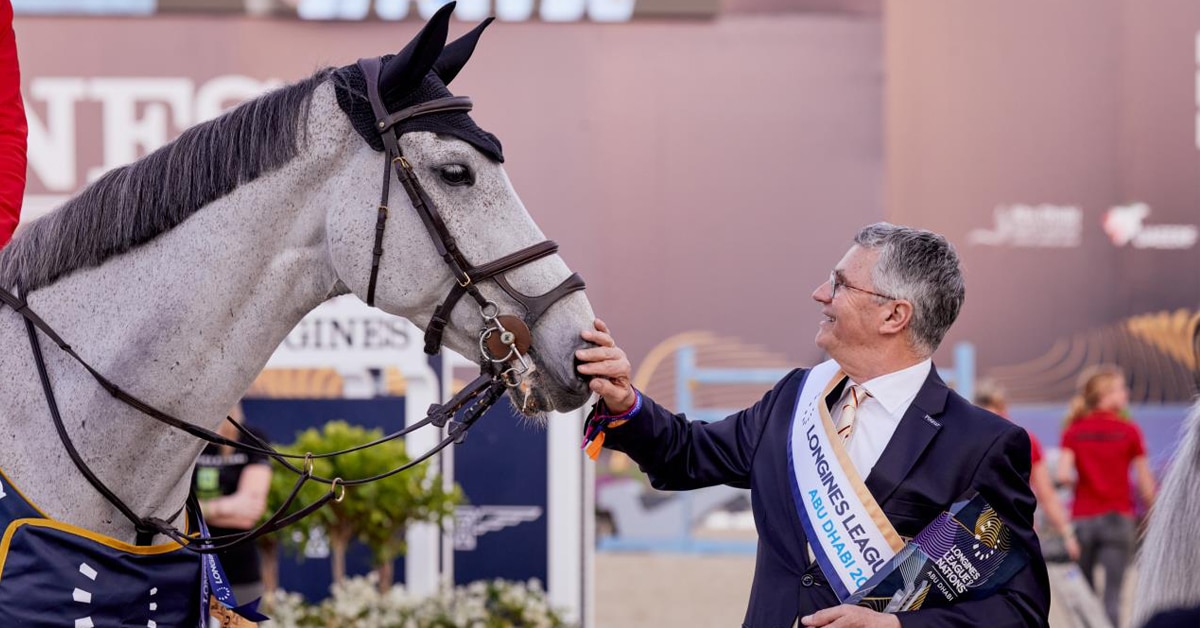 A smiling man holding a trophy and patting a grey horse.