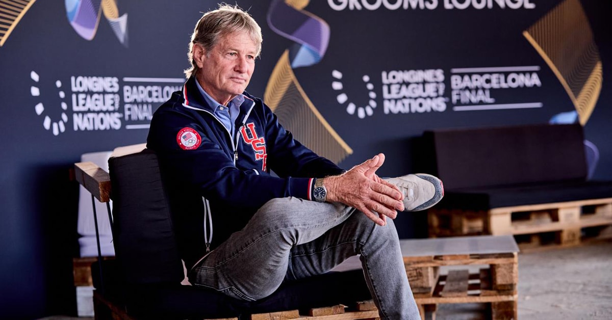 A man sitting on a bench in the stables at a horse show.