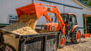 A Kubota tractor dumping manure into a container on a farm.