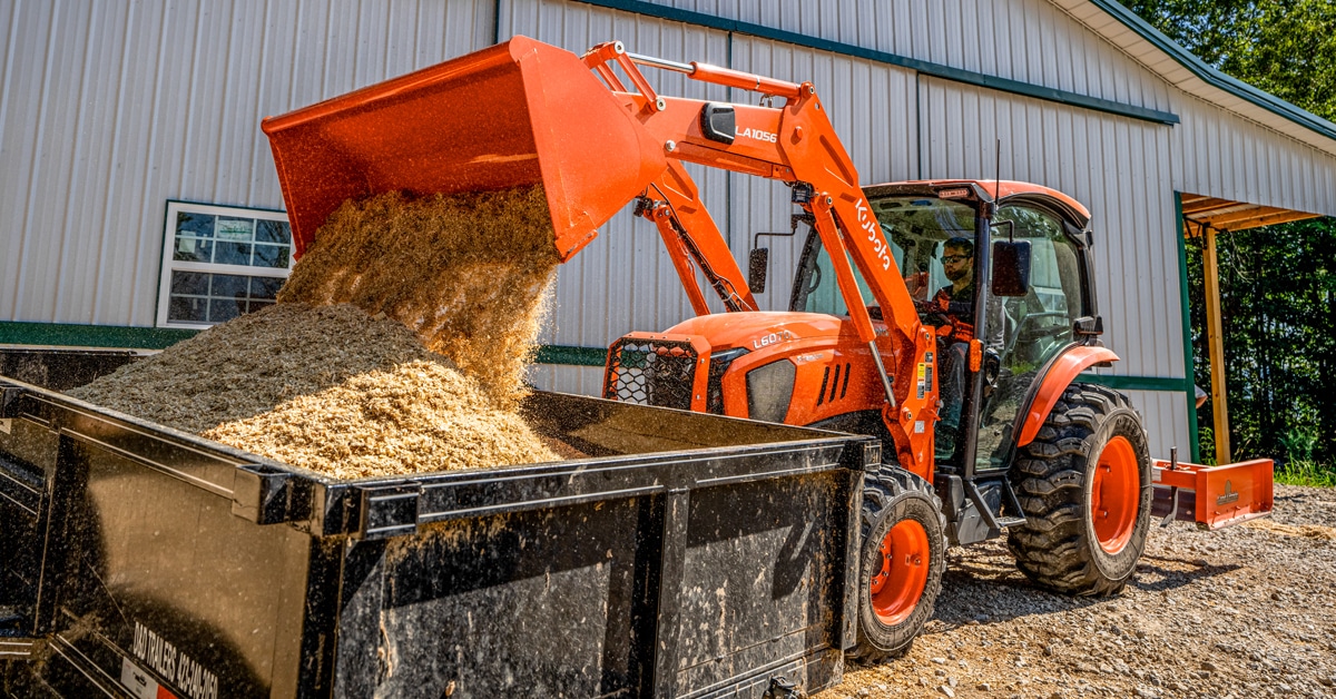 A Kubota tractor dumping manure into a container on a farm.
