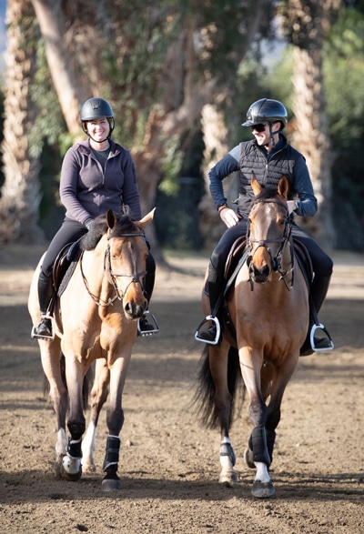 A man and woman riding bay horses down a dirt road.