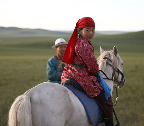 A young Mongolian girl on a grey horse.