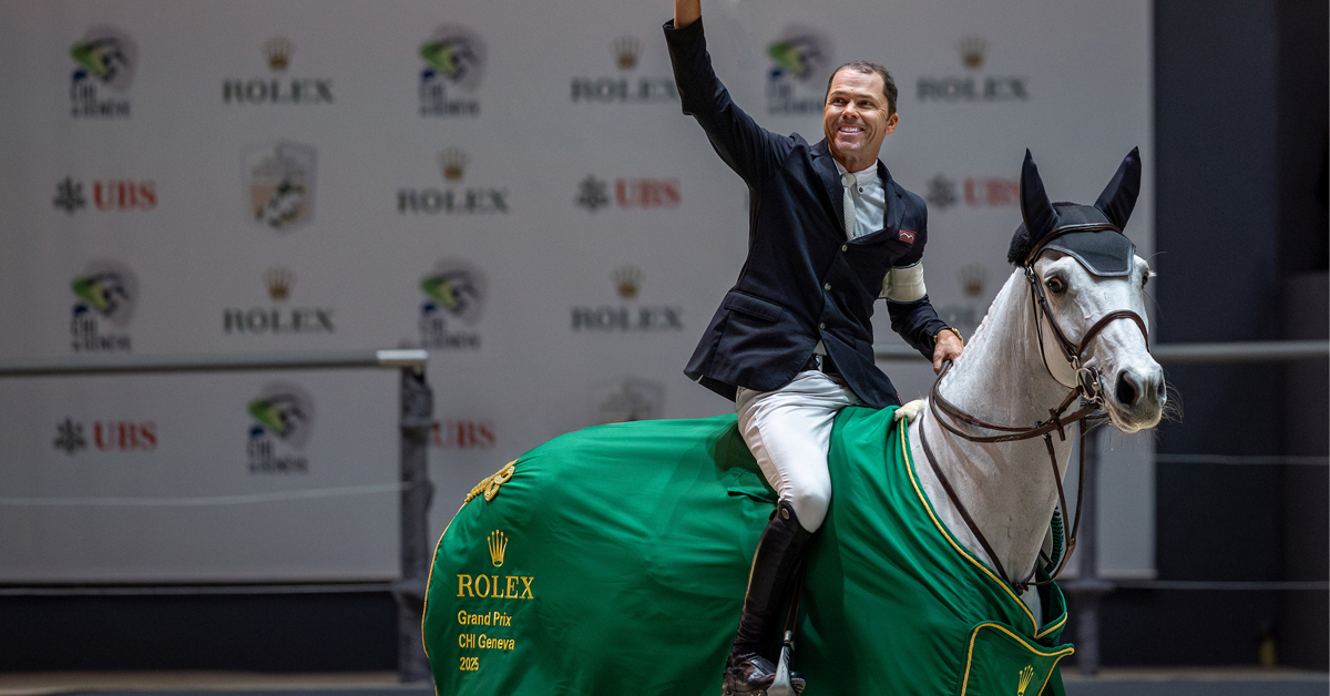 A man waving from the back of a grey mare that is wearing a Rolex cooler.