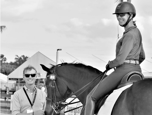 A black-and-white photo of a man standing with a woman on a horse.