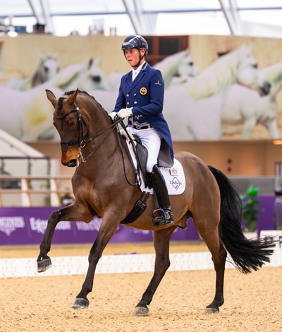 A man riding a bay dressage horse in flying change during a test.