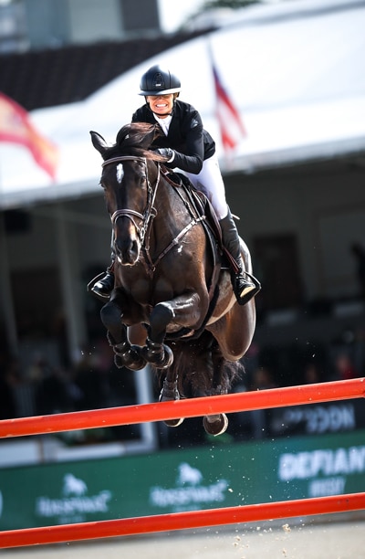 A woman riding a dark bay horse over a fence at WEF.