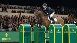 A man jumping a bay horse over a Rolex fence.
