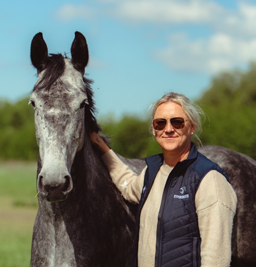 A blond woman patting a young grey horse.