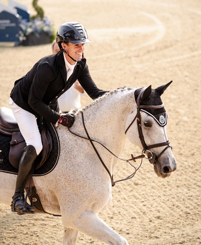 A man smiling an patting a grey horse in a jumping ring.