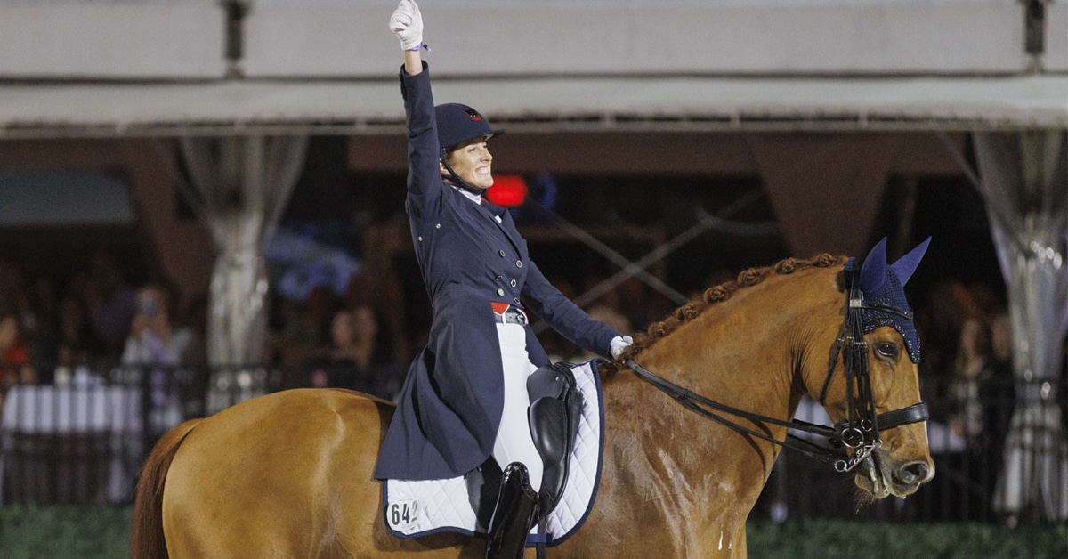 A woman on a dressage horse with her fist in the air in victory.
