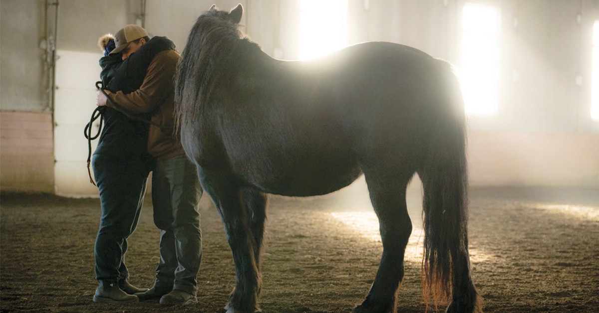 A couple hugging in an arena beside ahorse.