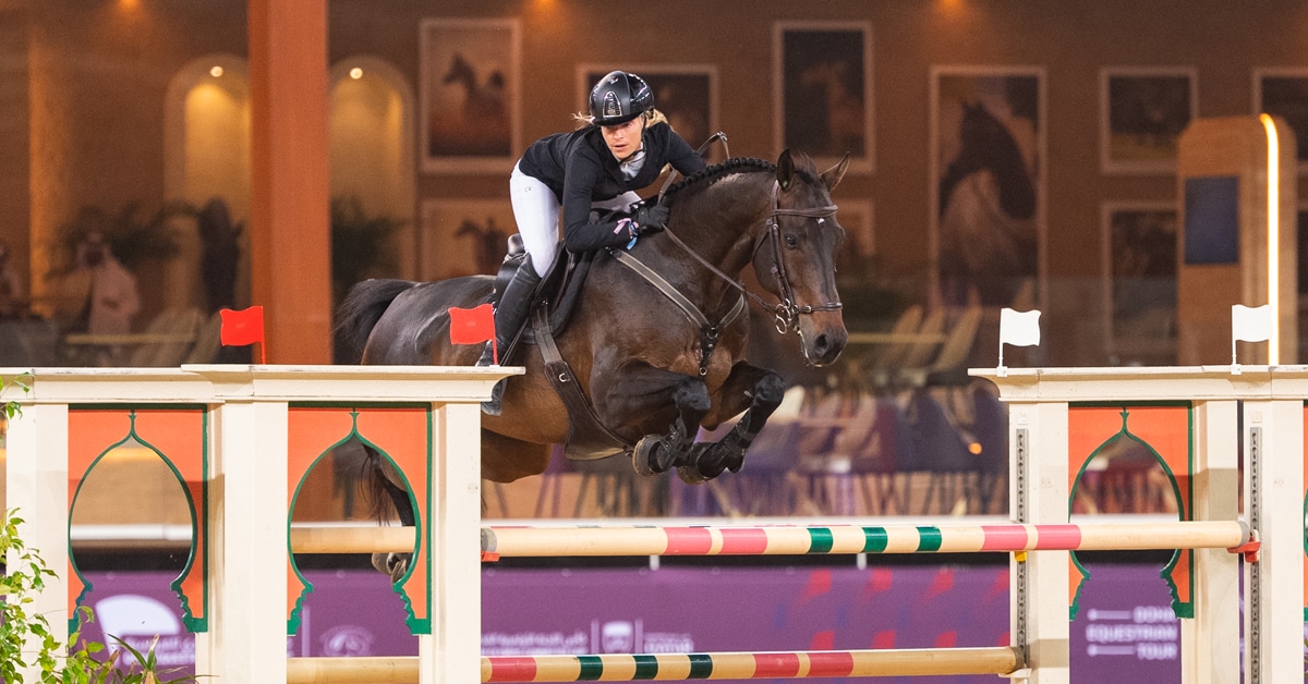 A woman jumping a bay horse over a fence in Doha.