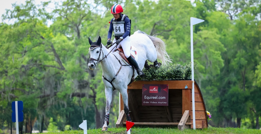 A woman jumping a grey horse over a cross-country fence.