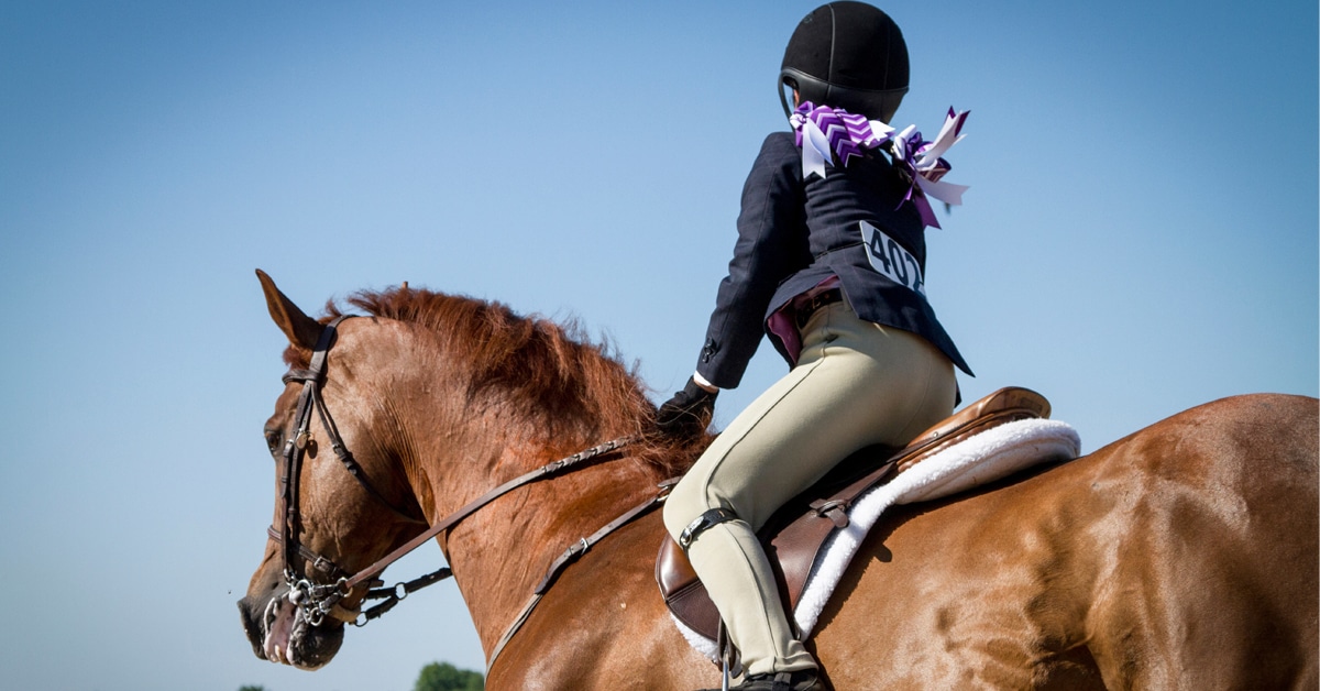 A young girl with bright hair bows riding in a show.