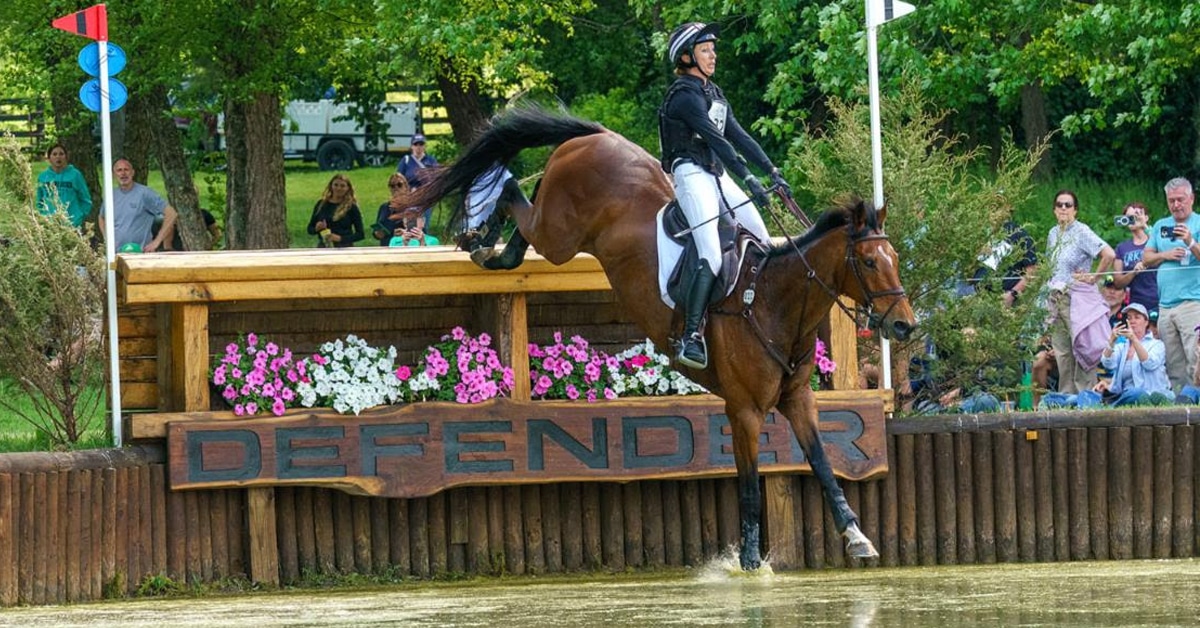 A woman jumping a bay horse into a water jump on cross-country.