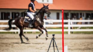 A horse and rider galloping past start timers at a show.