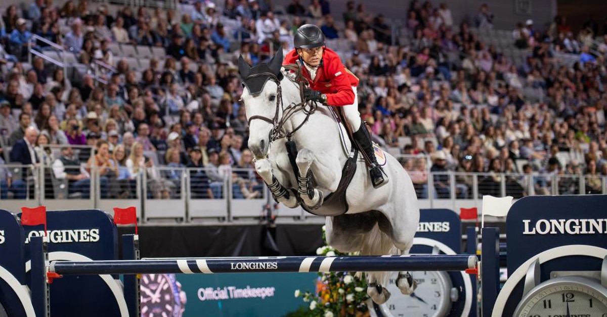 A man jumping a grey horse over a fence in a competition.