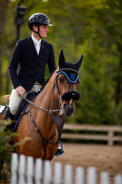 A young man in a warmup ring on a bay horse.