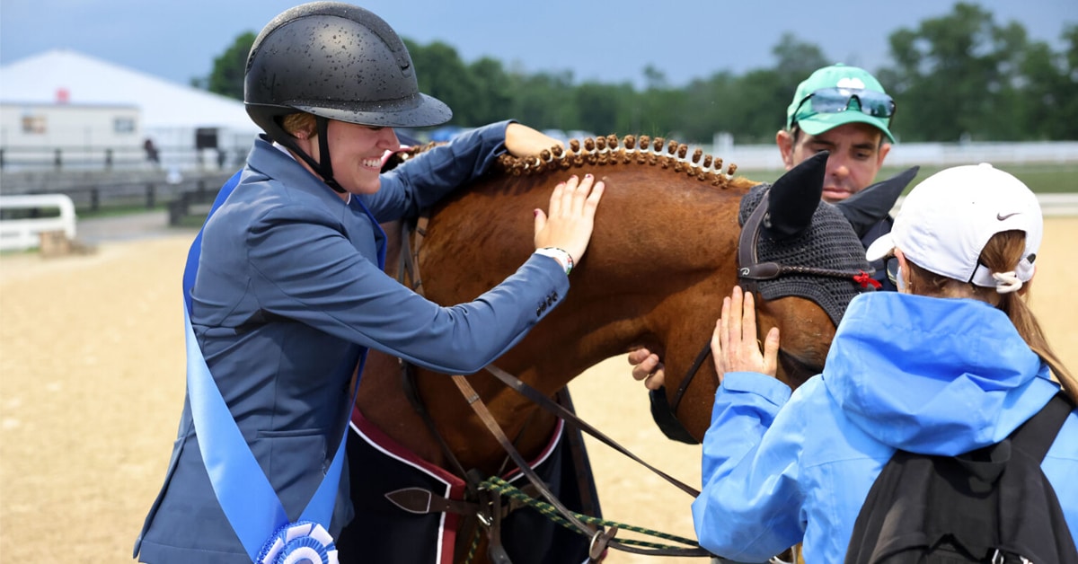 A woman petting a horse after winning a class.