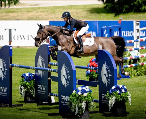 A woman jumping a bay horse over a fence at tbird.
