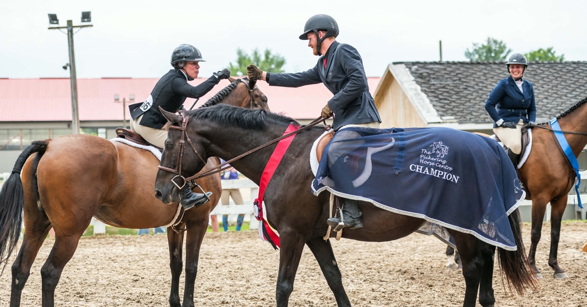 Two riders high-fiving at a smaller horse show.