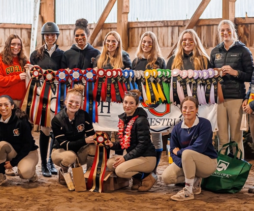 A group of smiling riders with horse show ribbons.