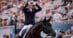 A woman on a dressage horse forming a heart with her hands.