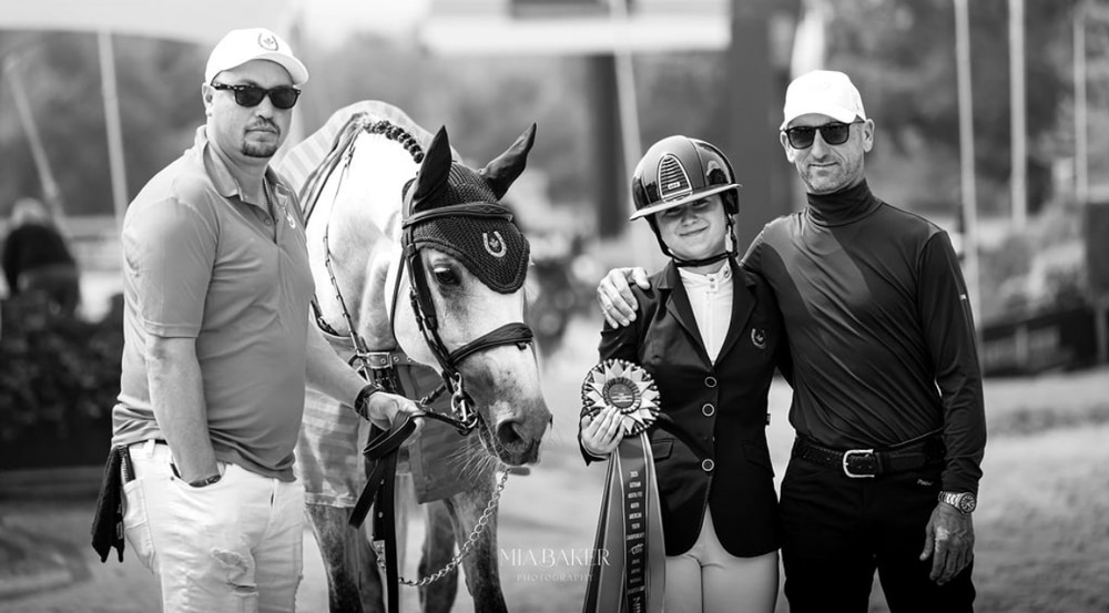 Two men and a teenager posing with a grey horse.
