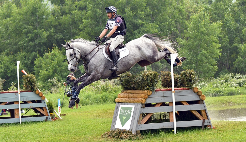A man jumping a grey horse over a cross-country fence at Bromont.