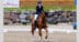 A smiling woman riding a bay horse during a dressage test.
