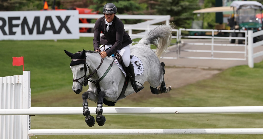 A man jumping a grey horse over a fence at Spruce Meadows.