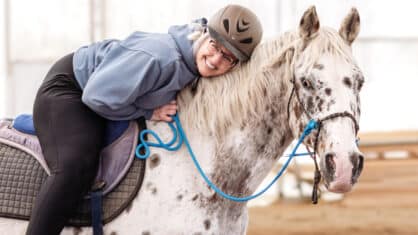 A smiling woman on a bitless spotted horse.