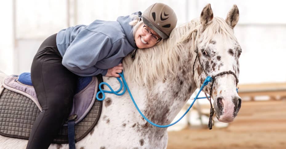 A smiling woman on a bitless spotted horse.