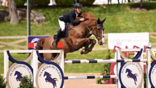 A young man jumping a chestnut horse over a fence during competition.