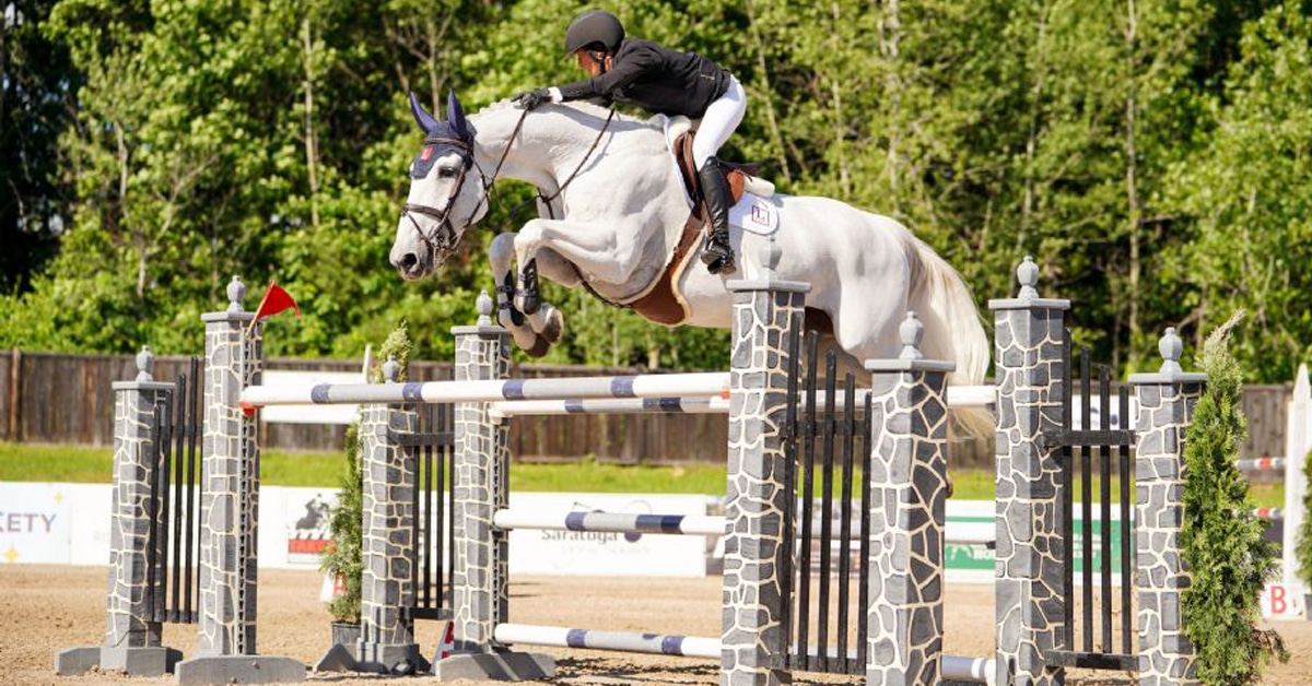 A woman jumping a grey horse over a fence in New York.