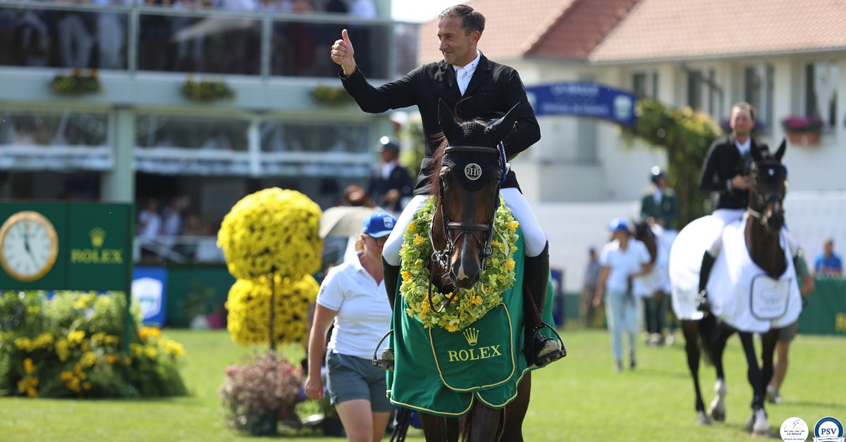 A man giving the thumbs-up on a bay horse during a prize-giving.