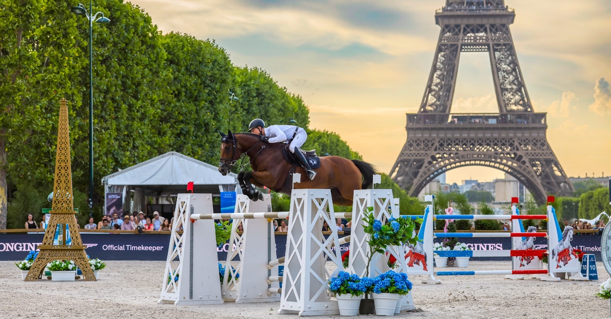 A man jumping a bay horse over a fence with the Eiffel Tower in the background.
