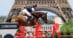 A man jumping a bay horse over a red fence with the Eiffel Tower in the background.