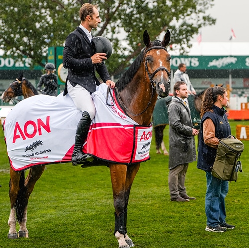 A man on a bay horse and his groom standing in the rain.