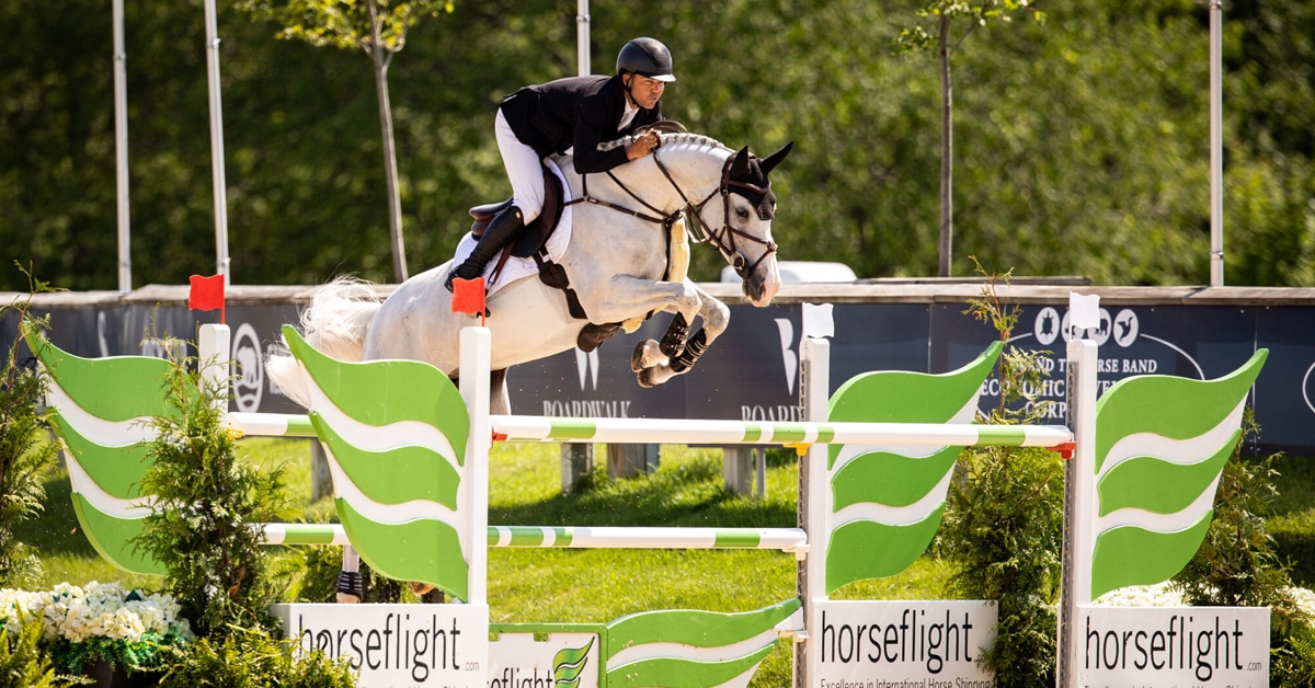 A man jumping a grey horse over a fence at Traverse City.