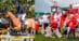 A man jumping a bay horse over a fence; a group of people dressed in Canadian flags.
