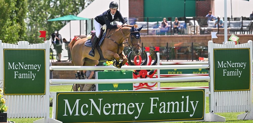 A young man jumping a chestnut horse over a fence at Spruce Meadows.