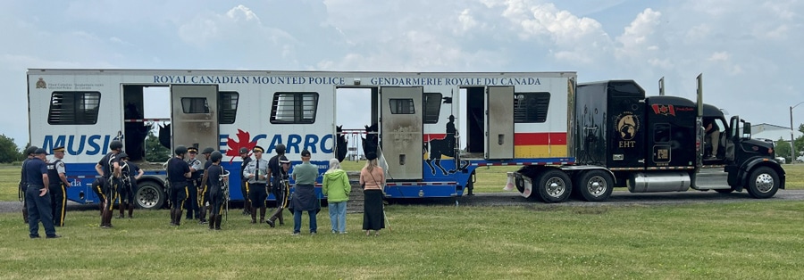 A group of people standing outside a large horse van.