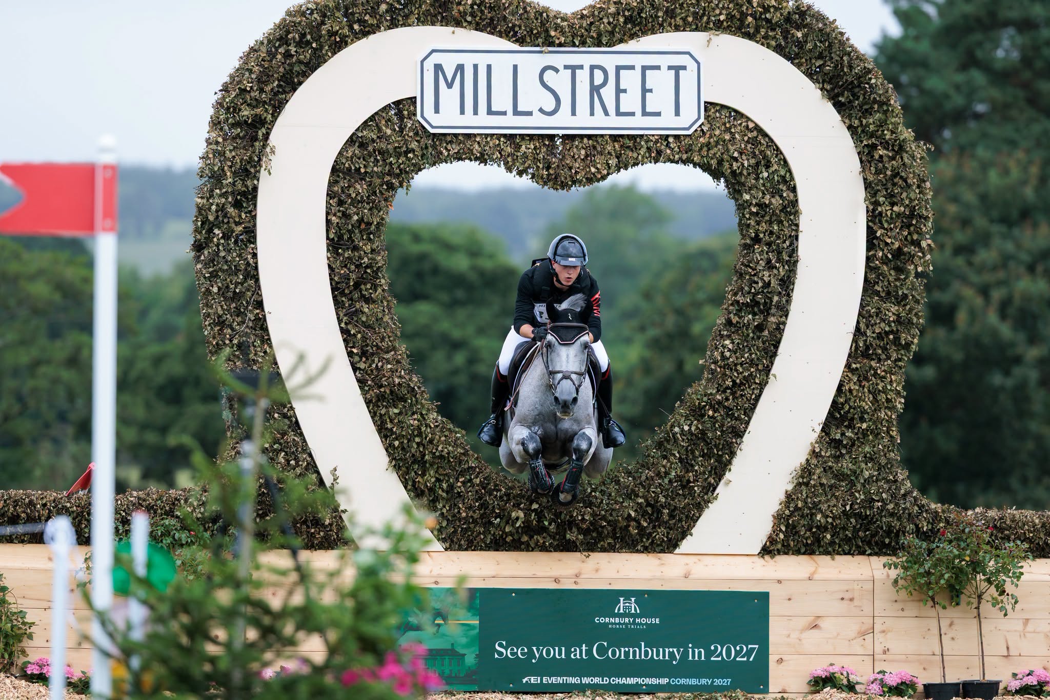 A young man on a grey horse jumping through a heart-shaped keyhole on cross-country.