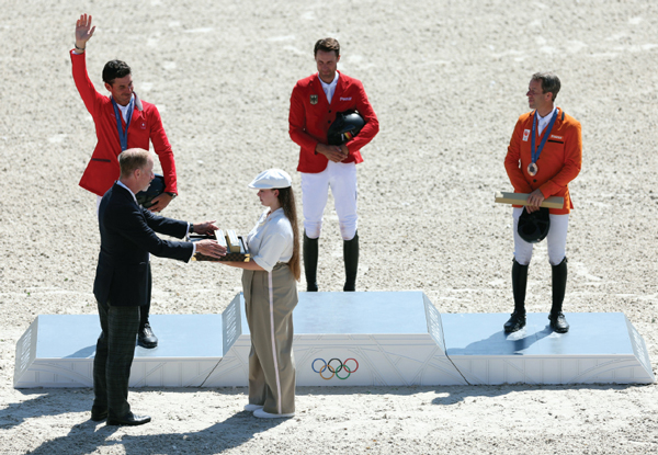Three riders on a podium receiving Olympic medals.