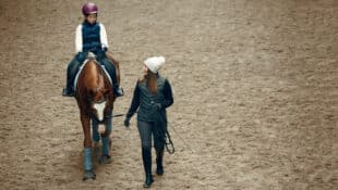 A woman coaching a young girl on a horse in an arena.