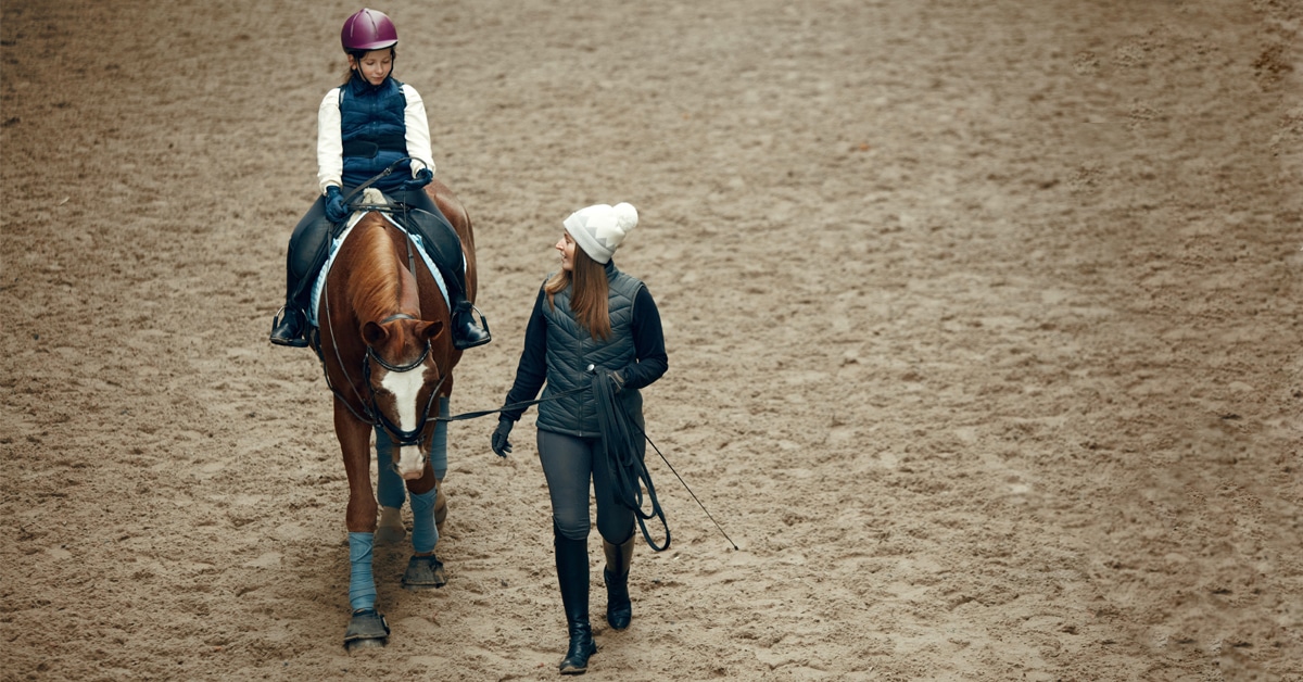 A woman coaching a young girl on a horse in an arena.