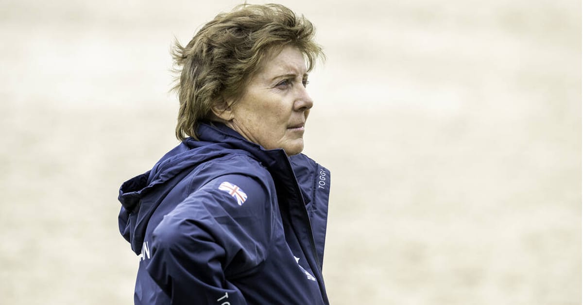 A woman standing in a jumping arena.